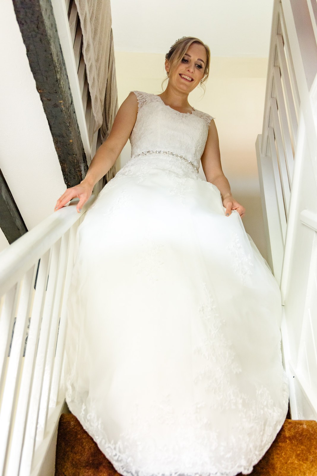 Bride gathering her full skirt as she descends a white painted staircase