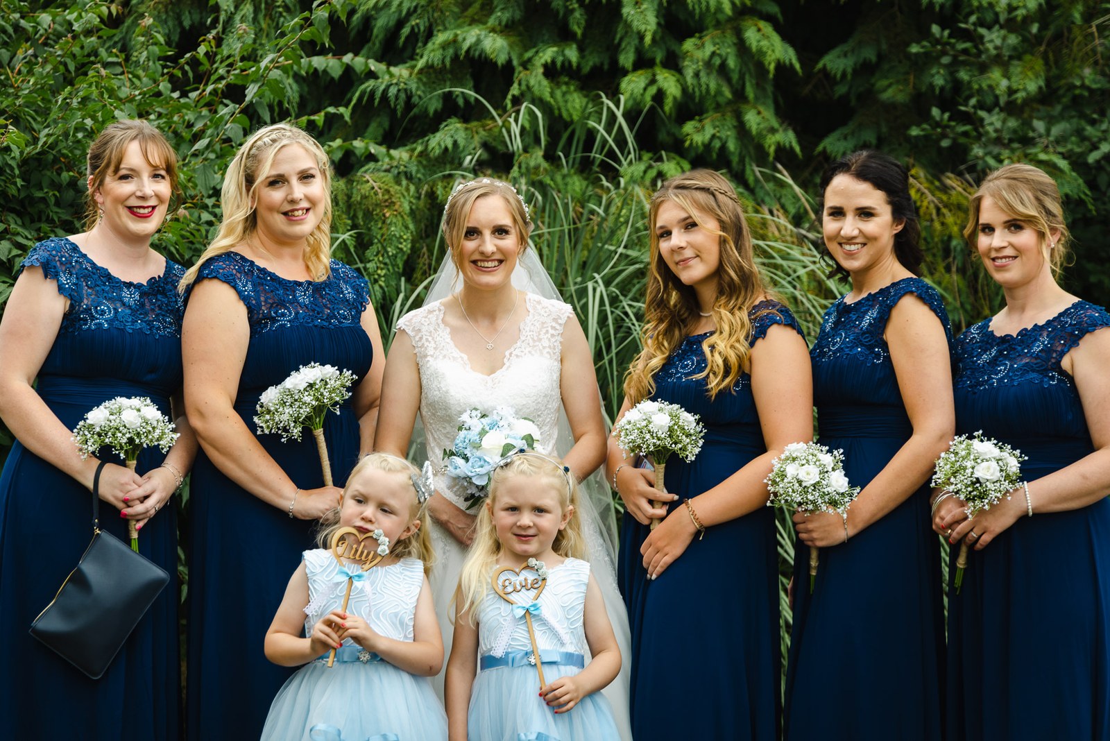 Bridesmaids in navy with two flower girls and a bride, holding gypsophila bouquets