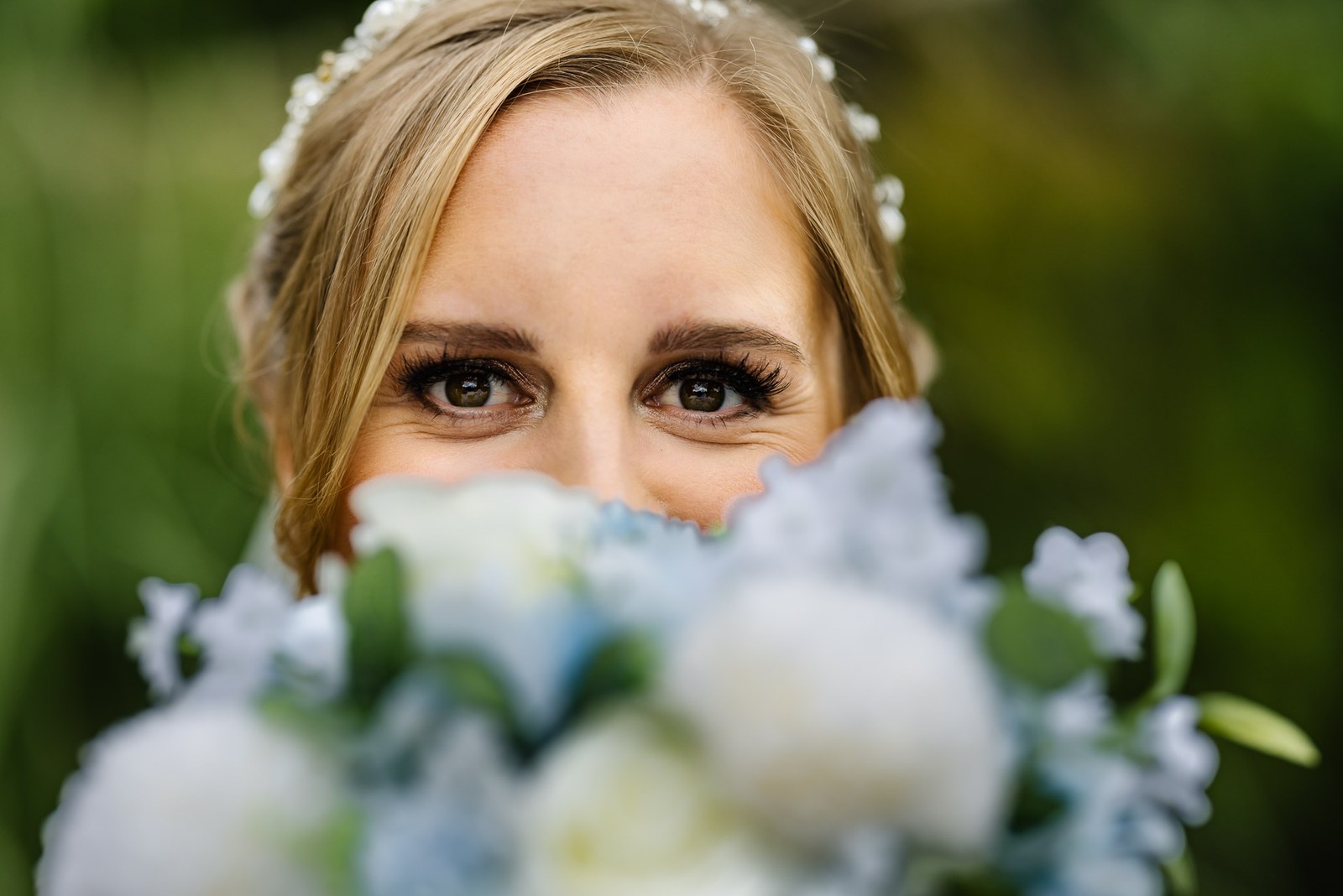 A bride's eyes peep over a posy of blue and white blooms