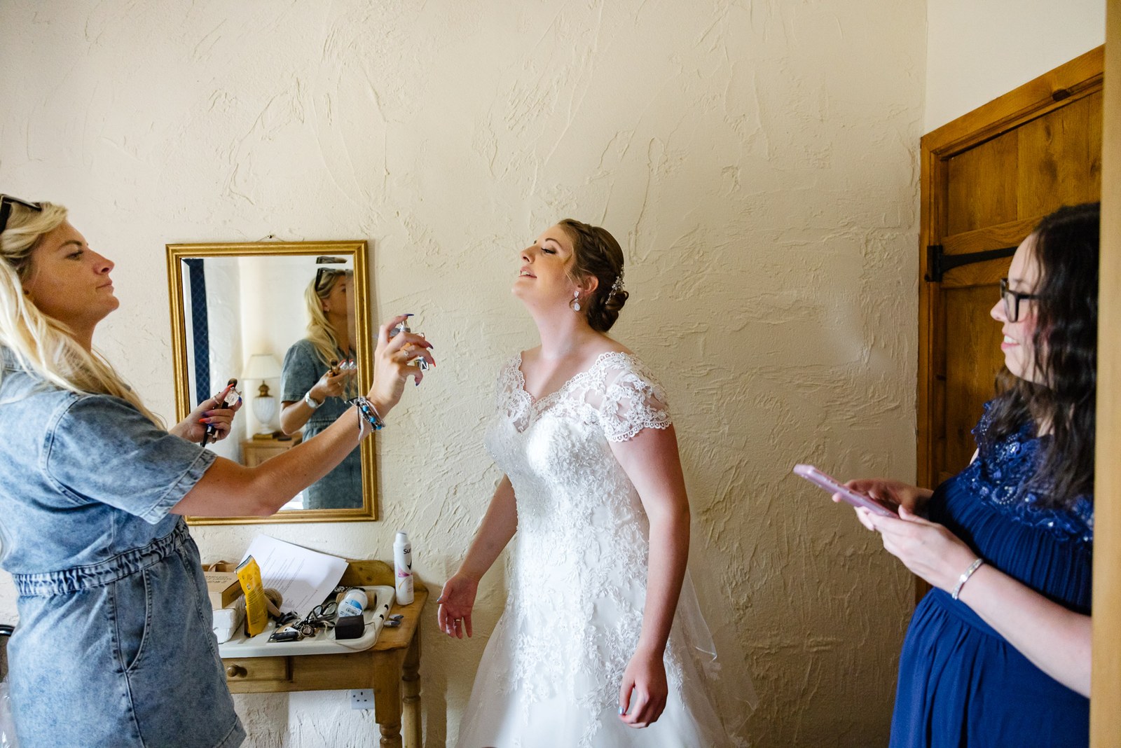 Bride having final touches while a helper photographs her by the mirror