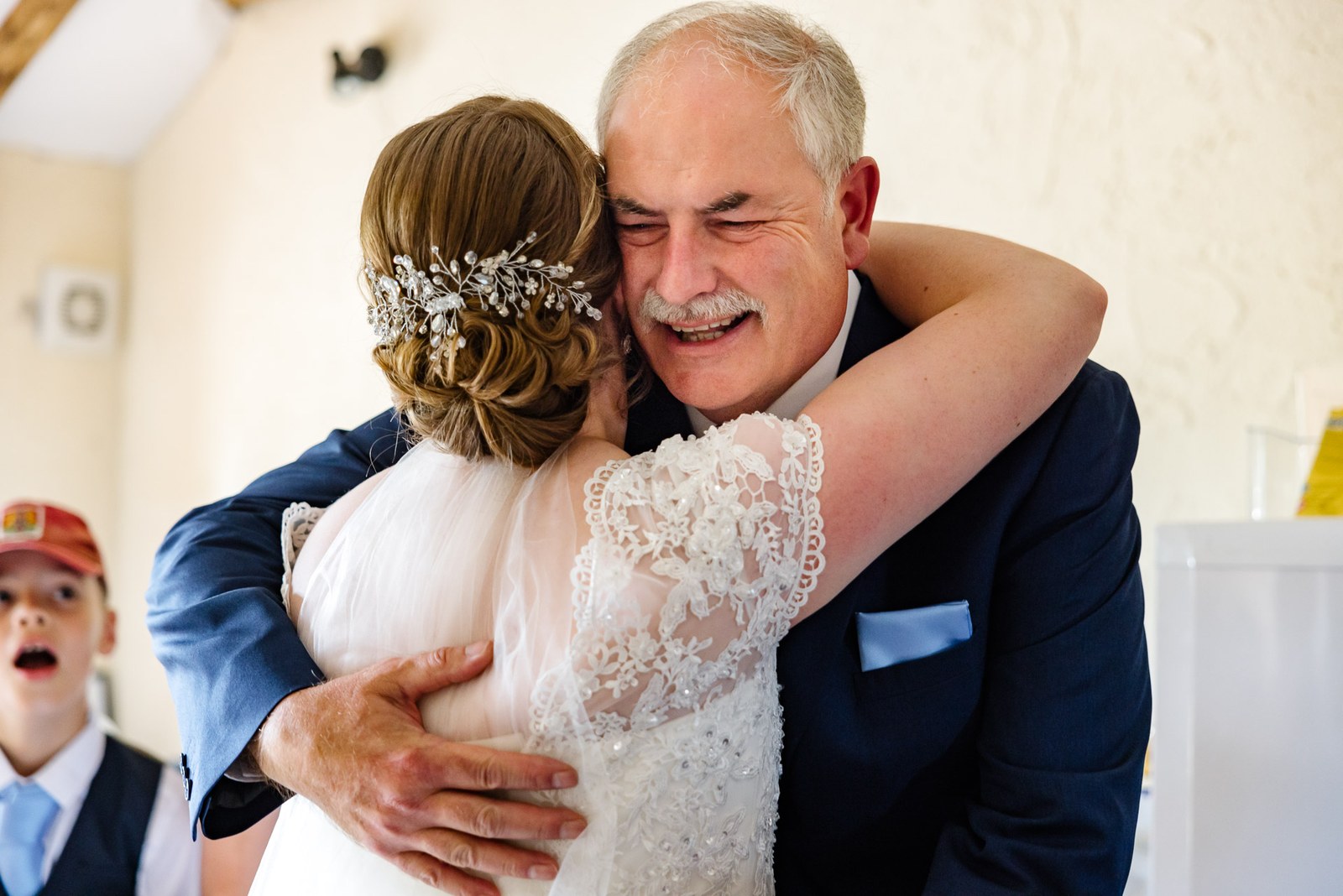 Bride embracing her father, who wears a navy three-piece suit