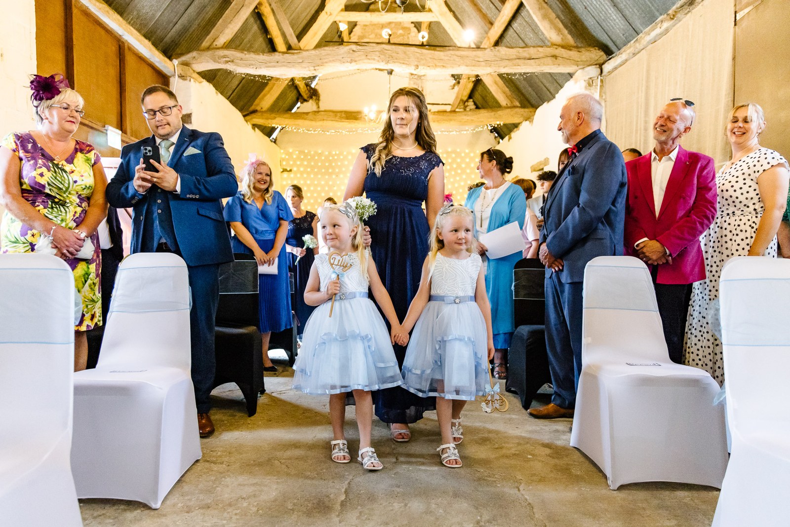Flower girls lead the procession down the fairy-lit barn aisle at Slapton Manor