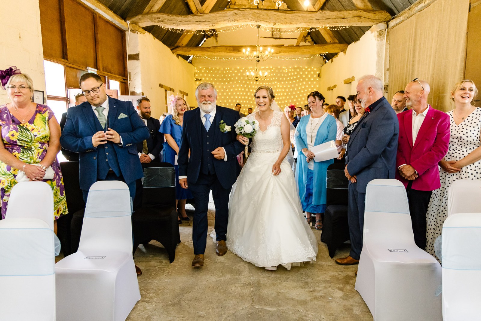 Bride on her father's arm walking the aisle through smiling guests