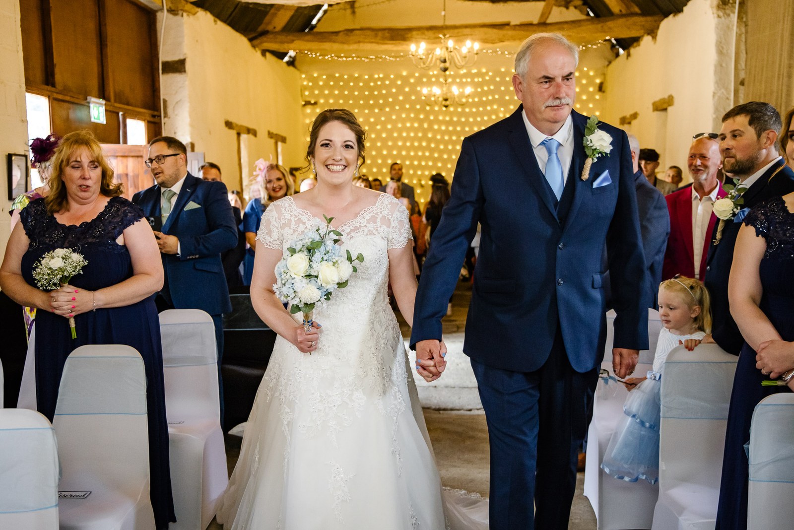 Bride walking the barn aisle with her father, bouquet in hand