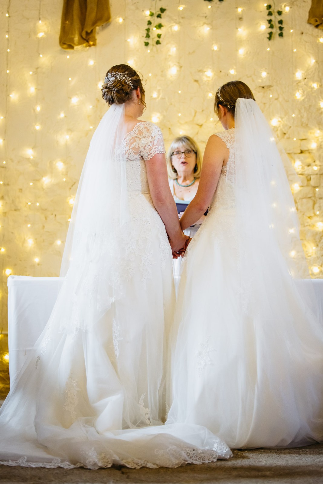 The couple hold hands before the celebrant against a wall of fairy lights