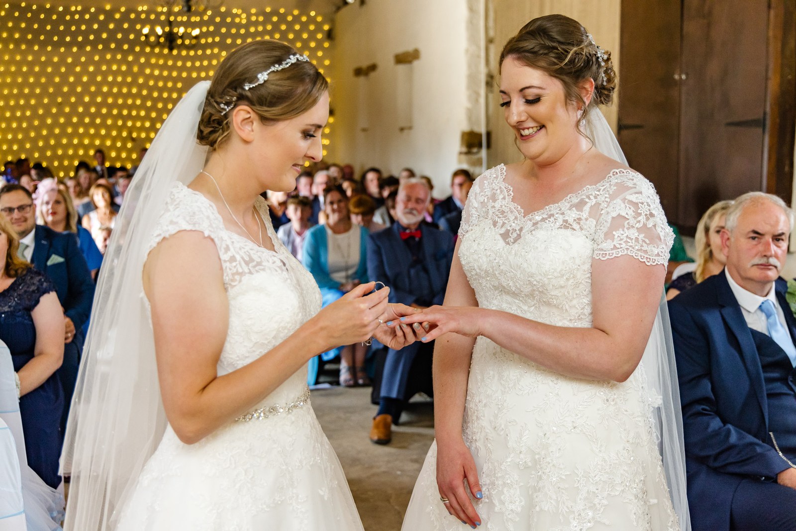 One bride slides a ring onto the other during the barn ceremony