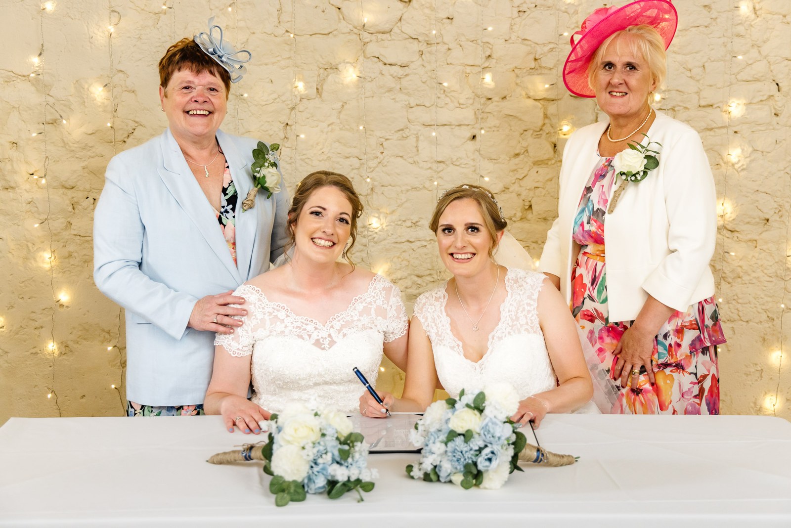 The two brides at the signing table flanked by their smiling mothers