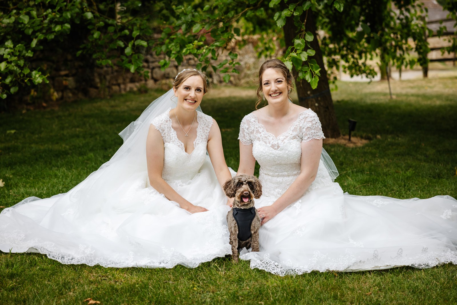 The newlyweds sit on the Slapton Manor lawn with their dog, dress trains fanned out
