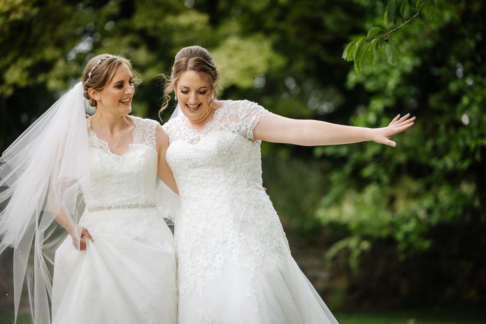 One bride flings an arm wide as the couple stroll across the grounds