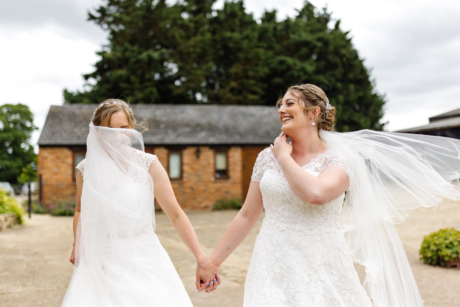 The newlyweds walk hand in hand past a brick barn at Slapton Manor