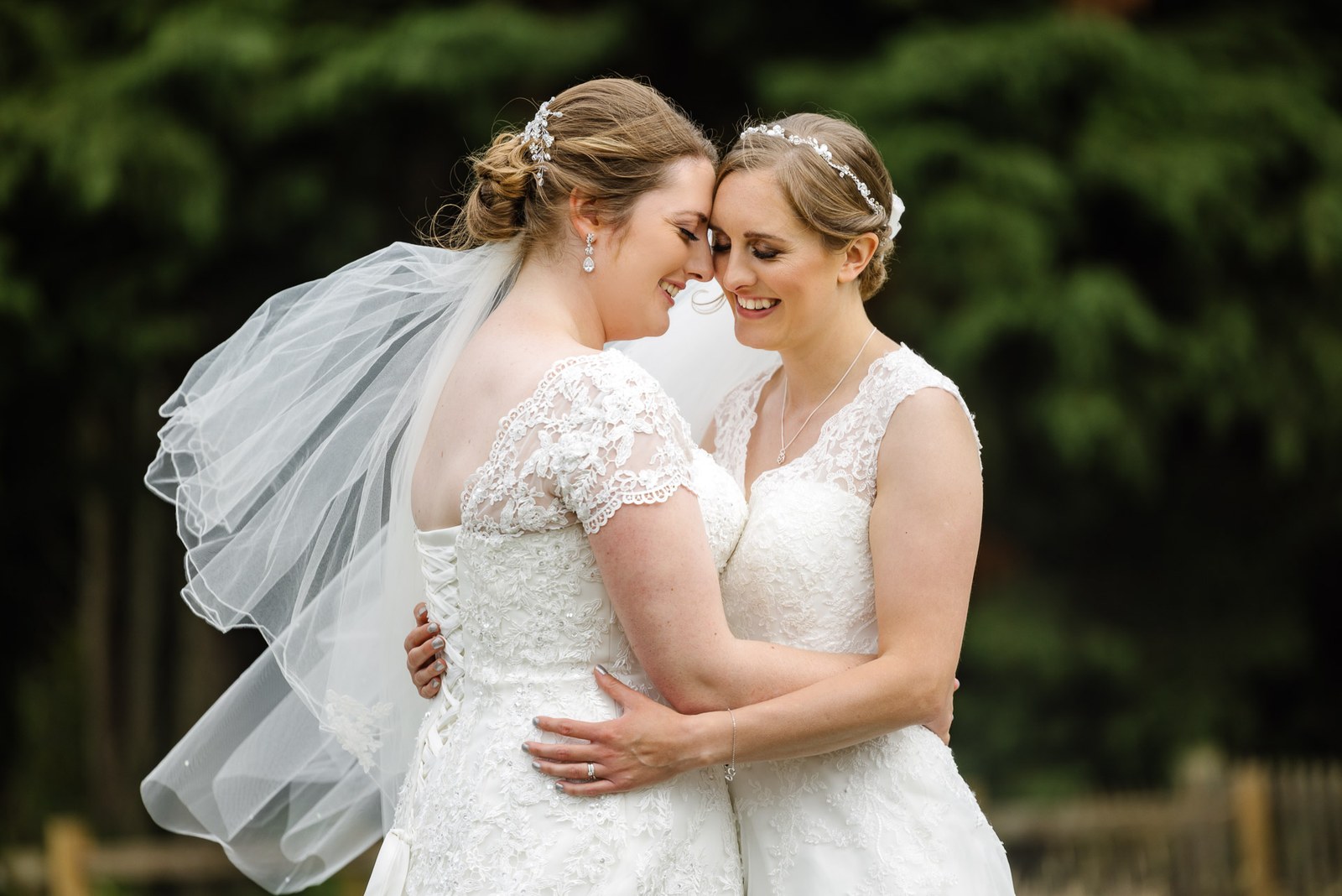 The two brides embrace, a veil catching the light behind them