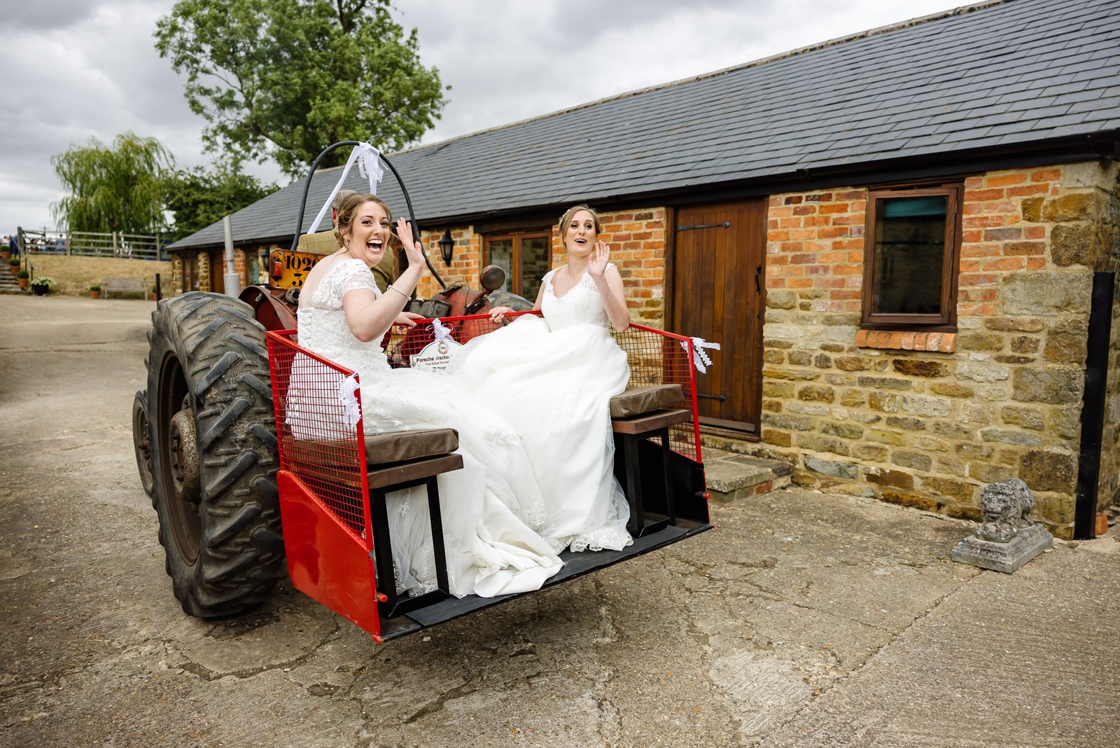 The two brides perched on the seat of a bright red vintage tractor trailer
