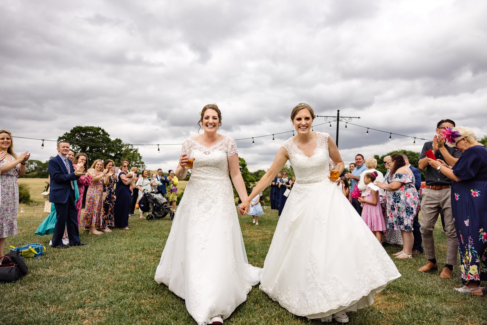 The couple walk through guests with drinks beneath festoon lights on the manor grounds