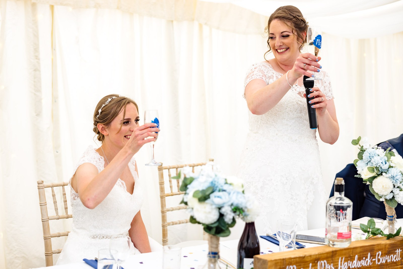 The two brides toast in the marquee, one still holding the microphone