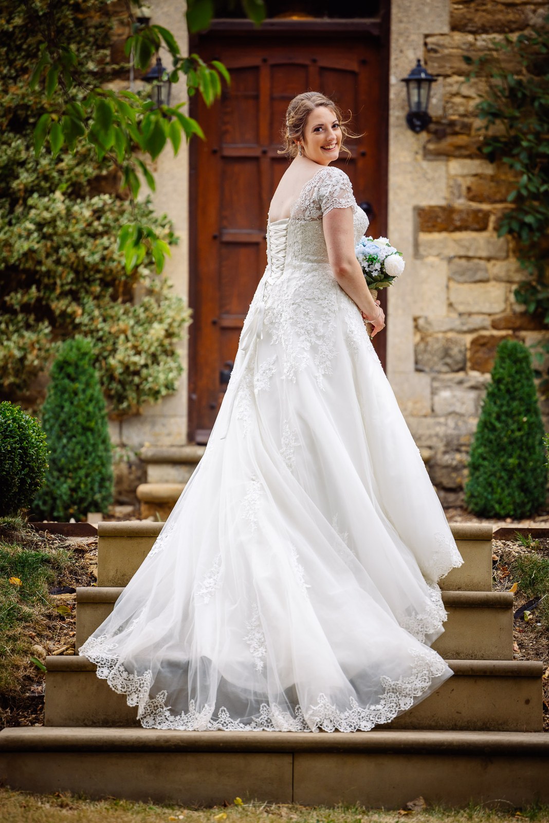 Bride poses on the steps before the tall timber door of Slapton Manor