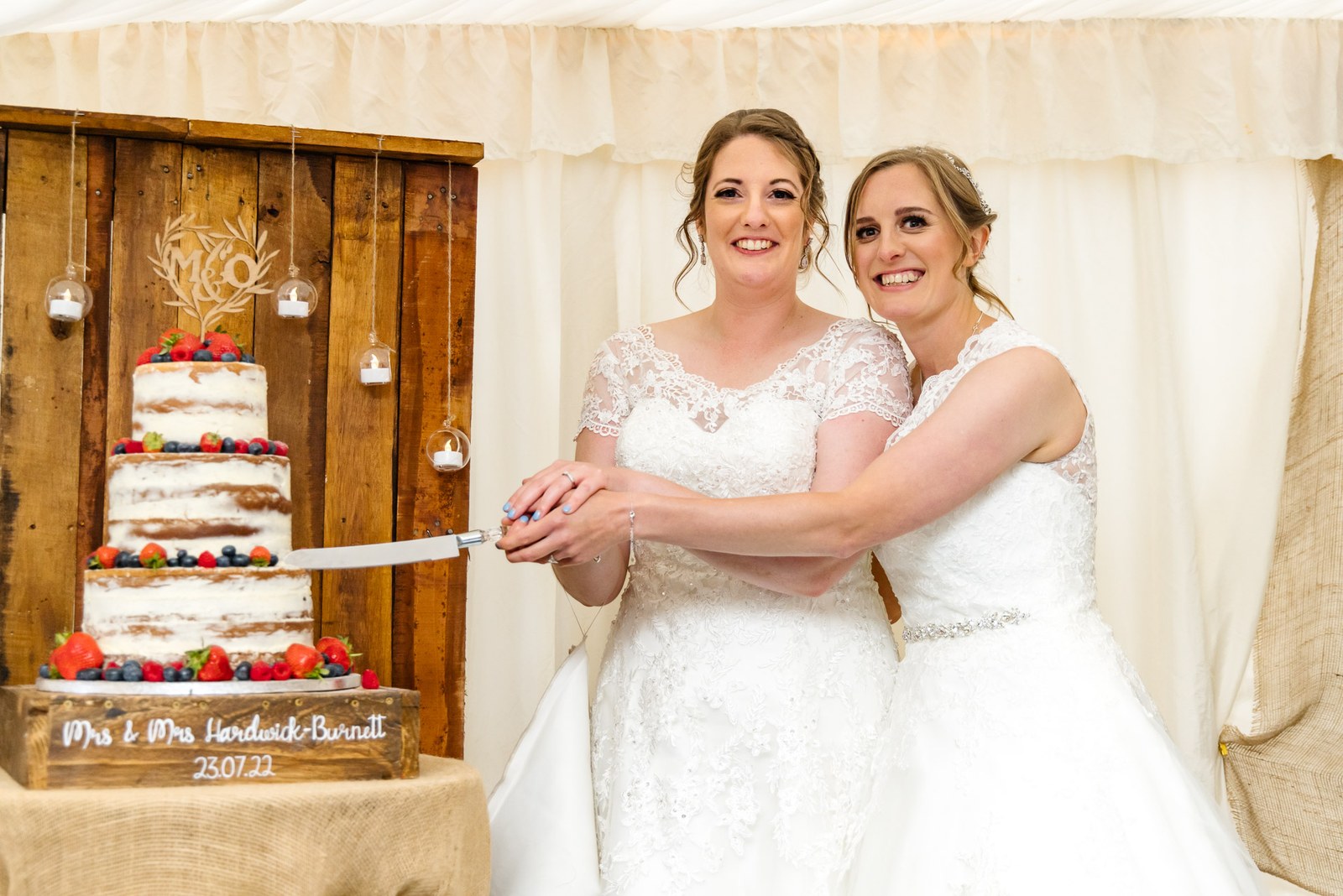 The newlyweds cut their berry-topped cake against a rustic marquee backdrop