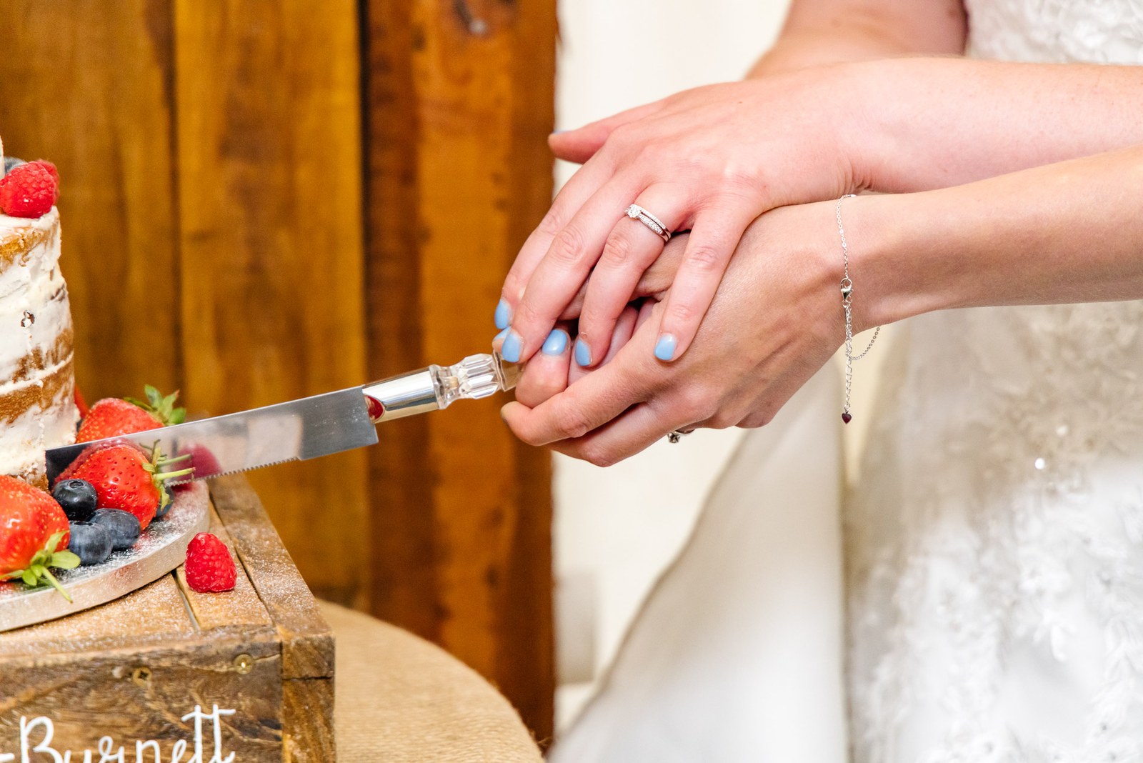 Close-up of the brides' ringed hands together on the cake knife