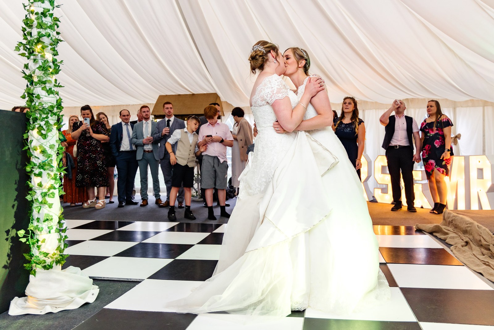 The two brides kiss during their first dance on the marquee's chequered floor