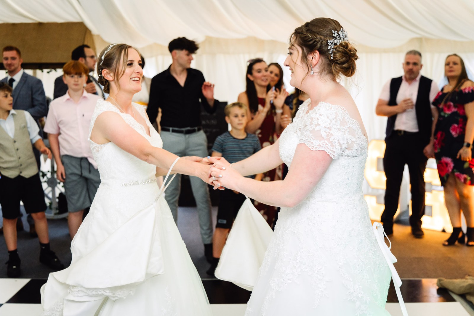 The couple hold hands in their first dance as guests watch in the marquee