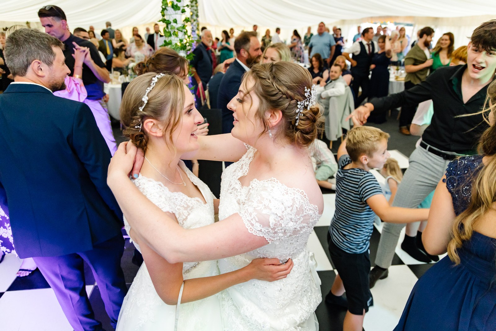 The two brides dance closely together among guests on the floor
