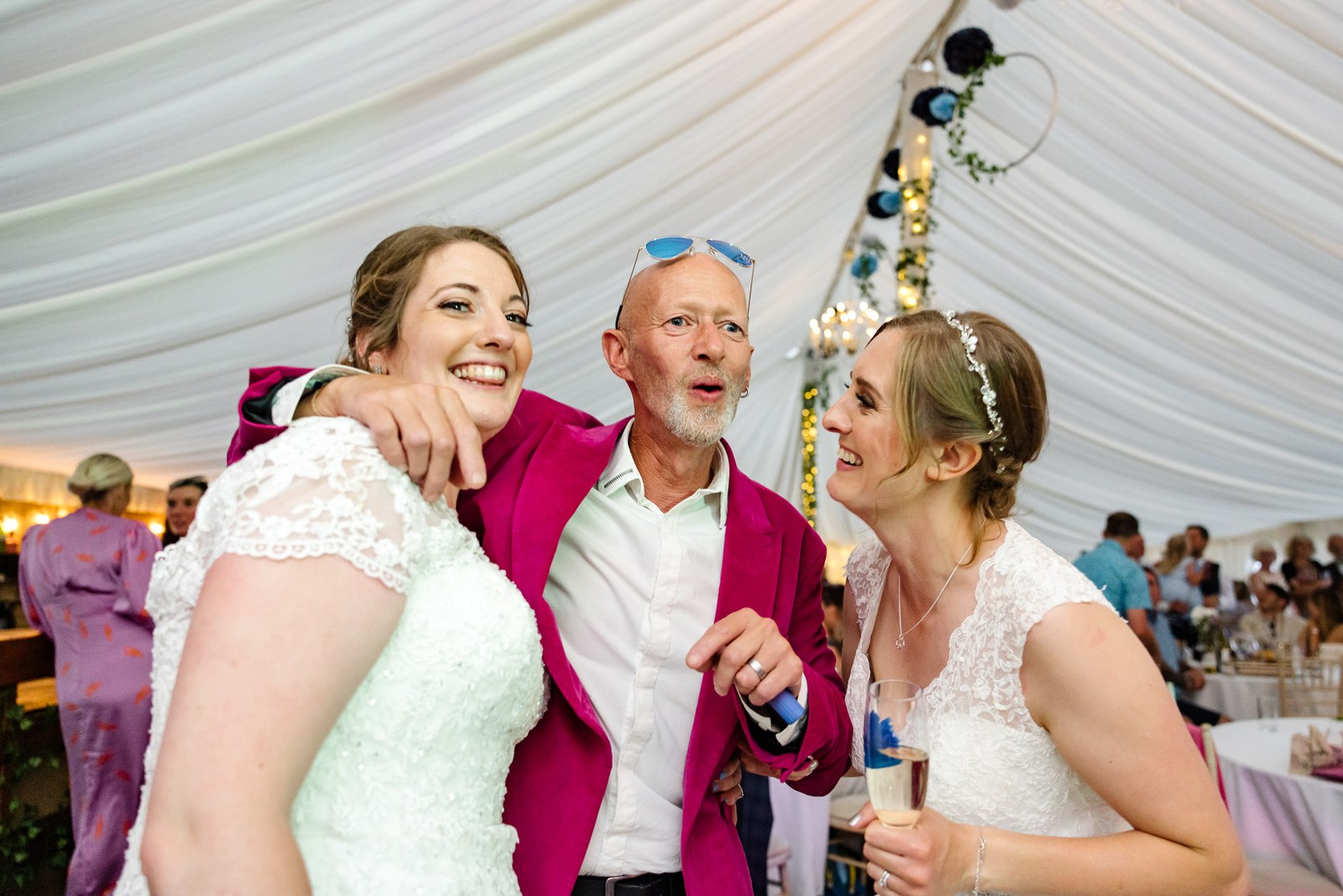 The newlyweds flank a laughing guest in a bright pink jacket