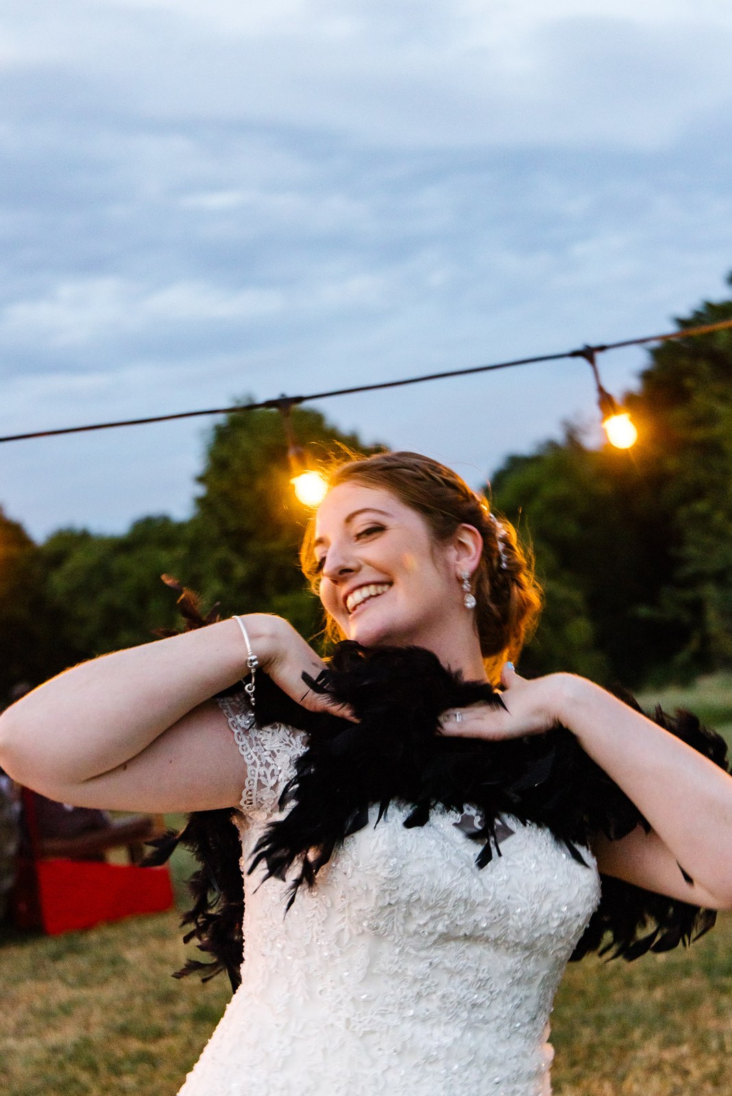 A guest swings a black feather boa under festoon lights at dusk