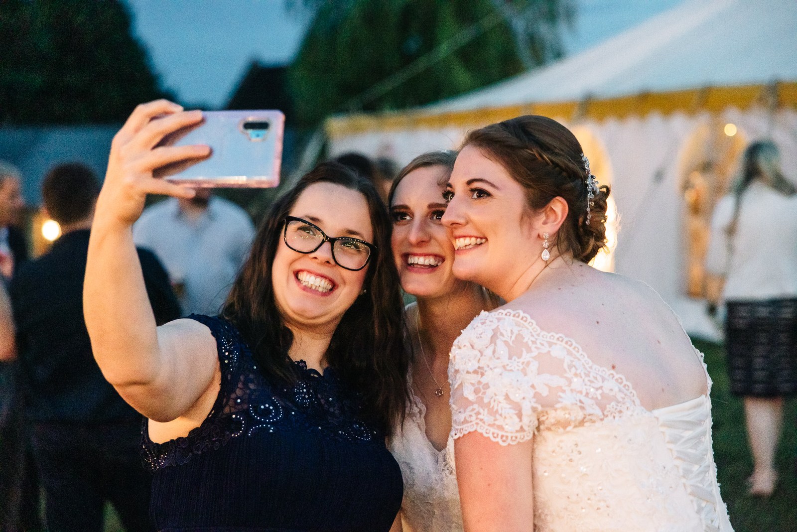 A guest takes a selfie with the two brides in the evening light
