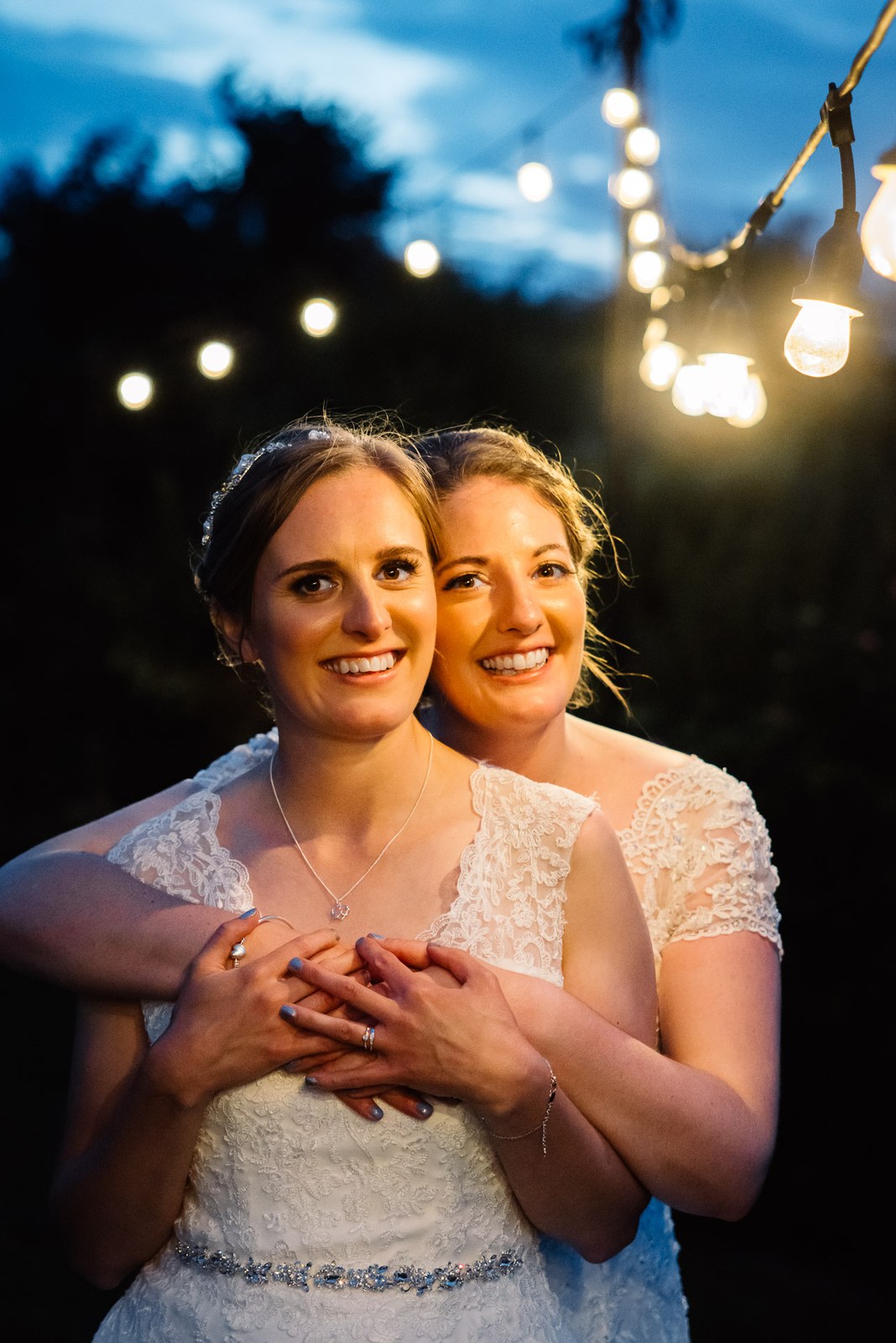 Evening portrait of the couple, one bride wrapping arms around the other