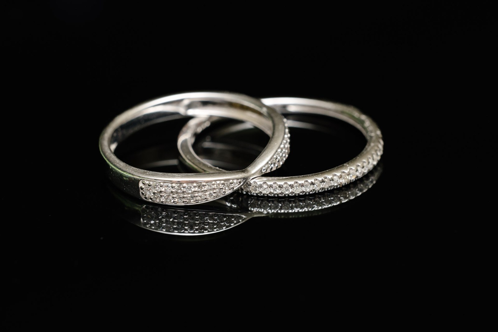 Two diamond-set wedding bands resting on a dark reflective surface