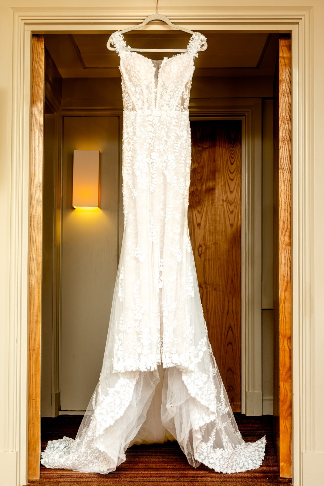 Lace fishtail wedding gown hanging in a panelled doorway of the suite