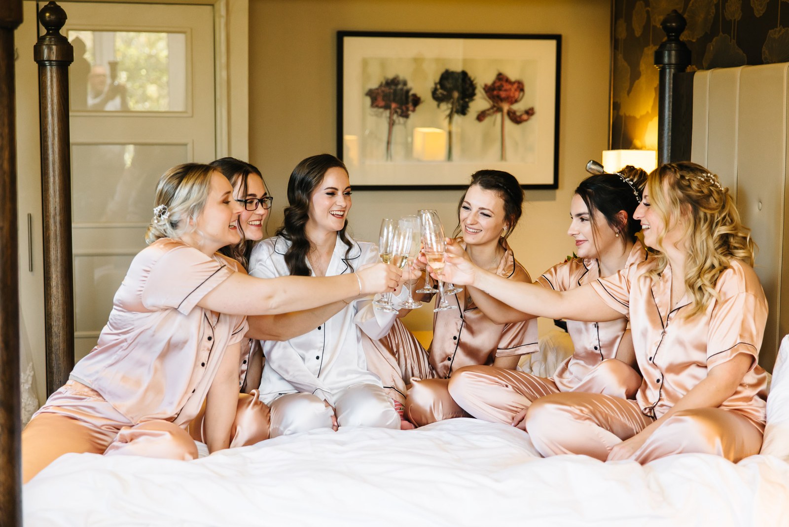 The bride and her bridesmaids toast with fizz across the bed in matching pyjamas