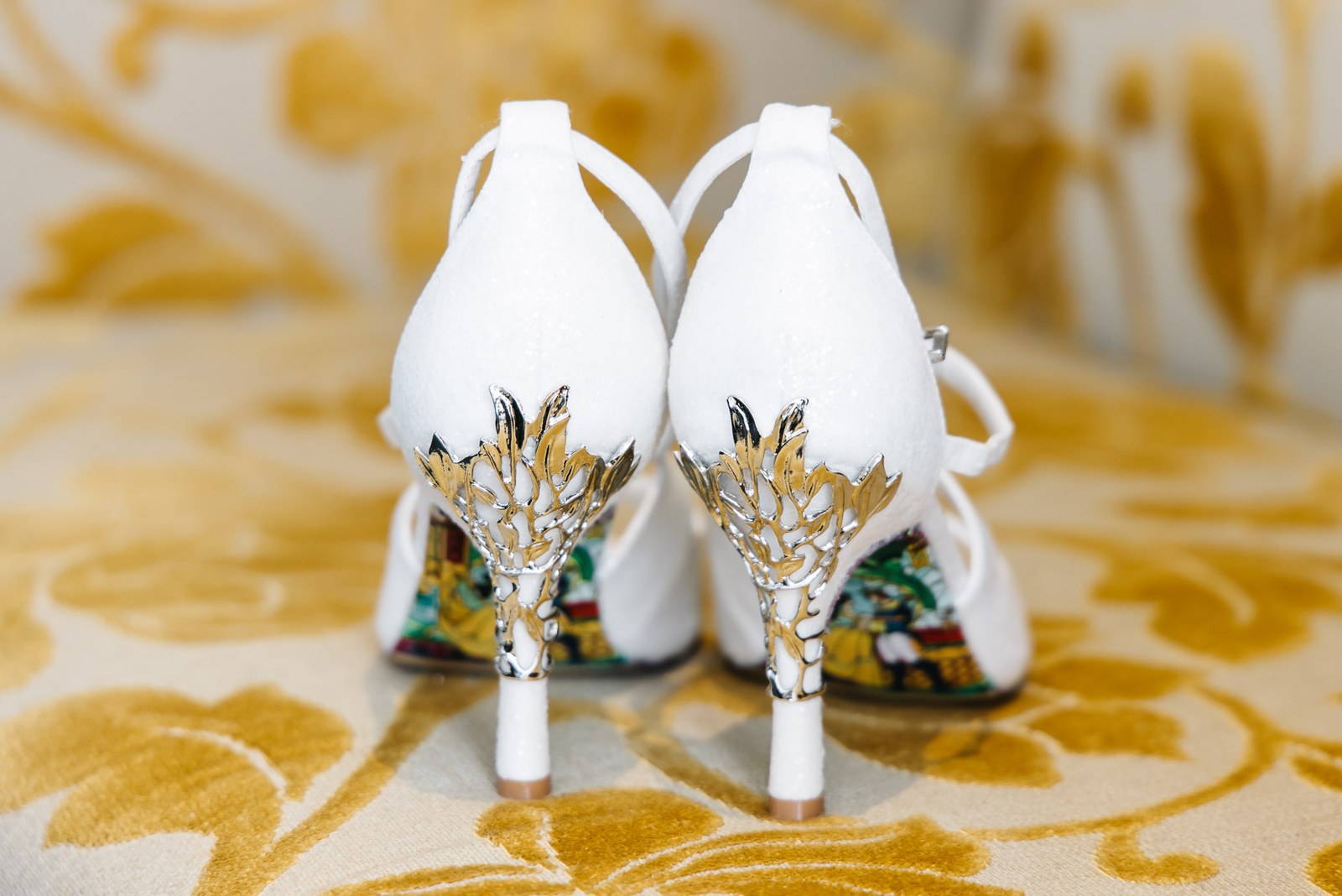 Close-up of white heels with gilded leaf detail on the golden carpet
