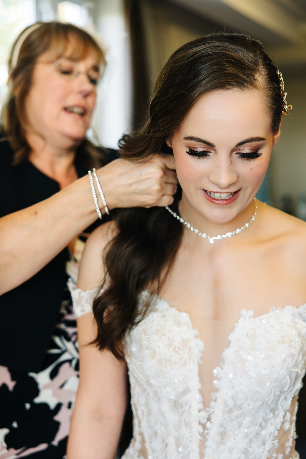 Mother of the bride fastens a necklace at the bride's neck during preparations