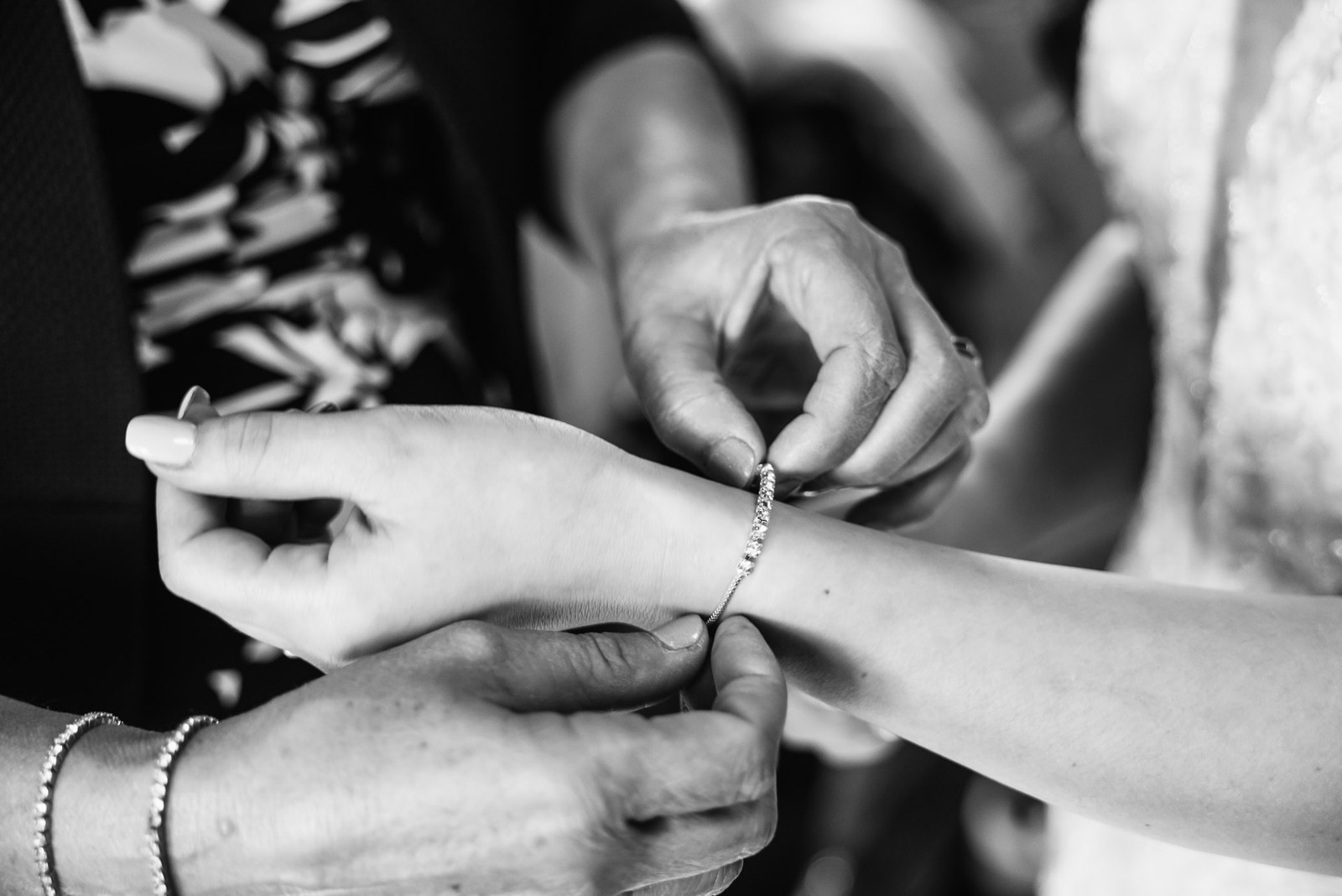 Close-up in monochrome of a bracelet being clasped onto the bride's wrist