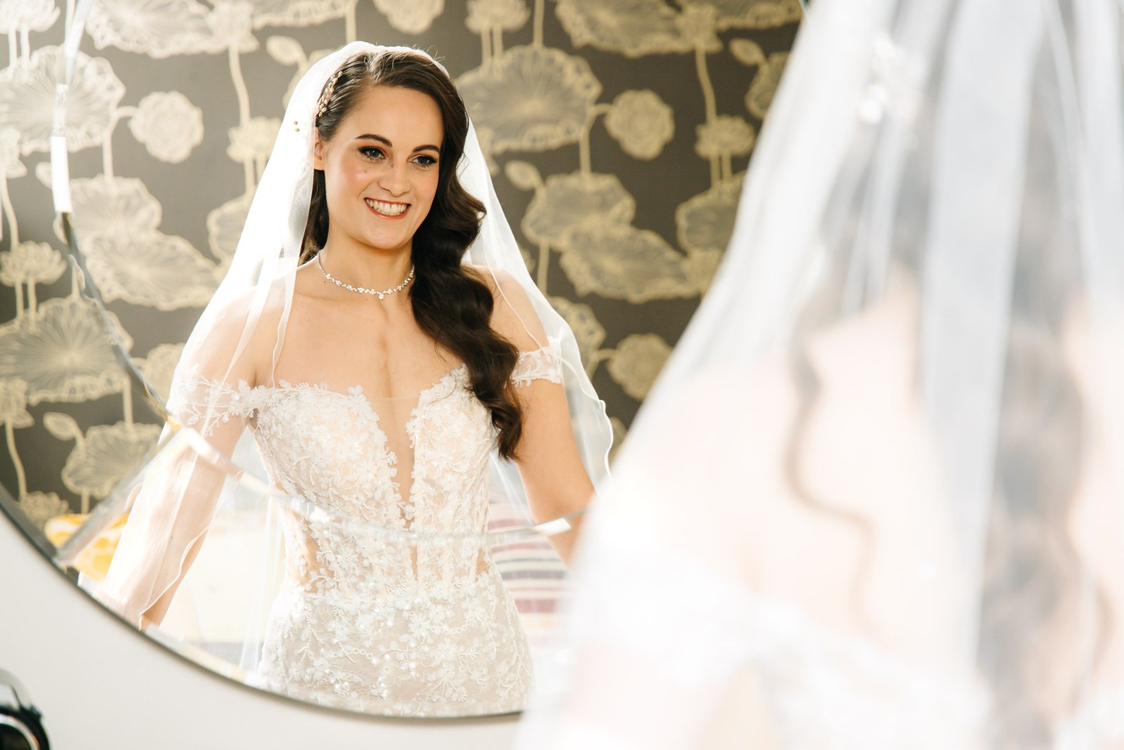 Bride in her veil reflected softly in a round mirror
