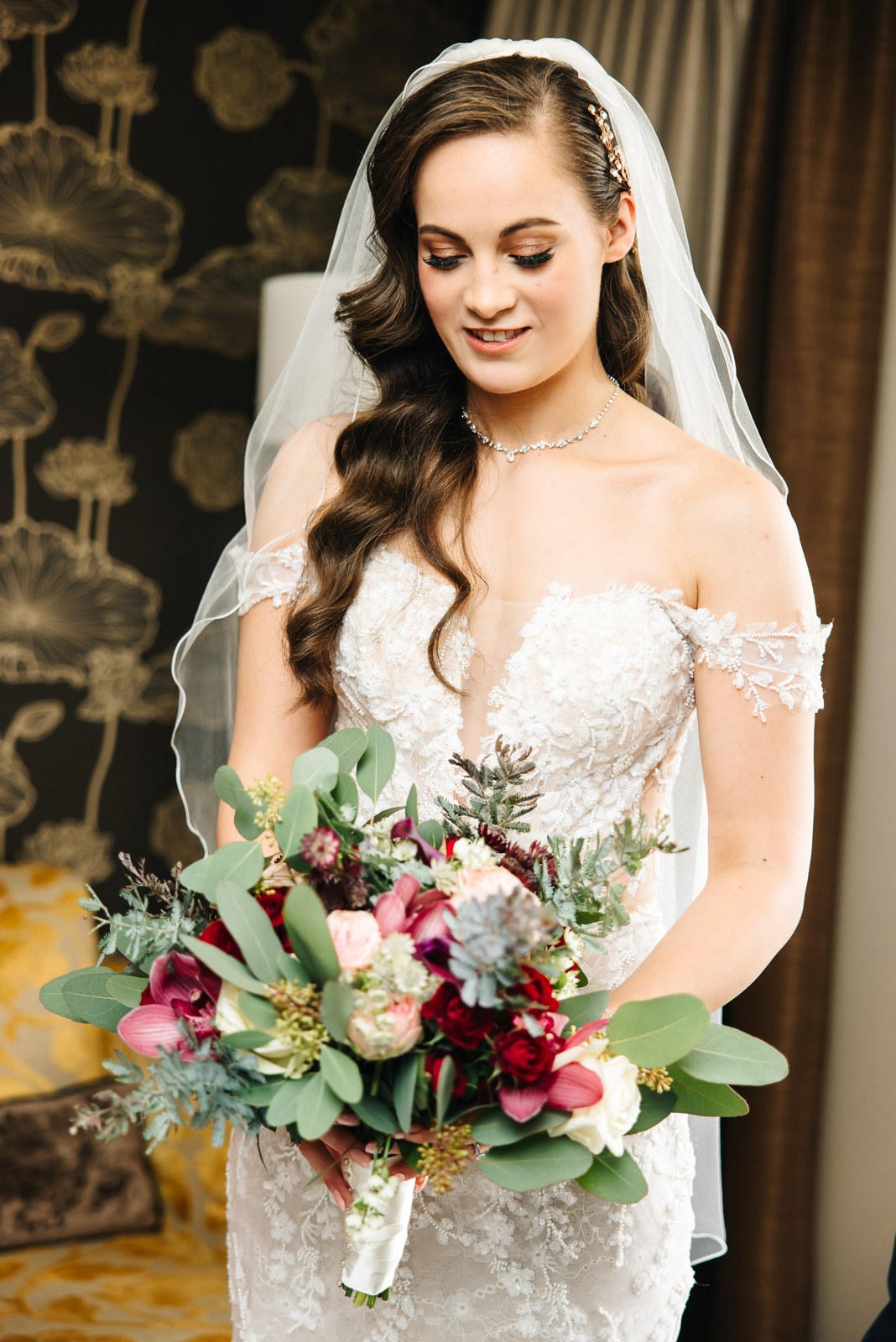Bride holding an autumnal bouquet of burgundy and blush blooms in her veil