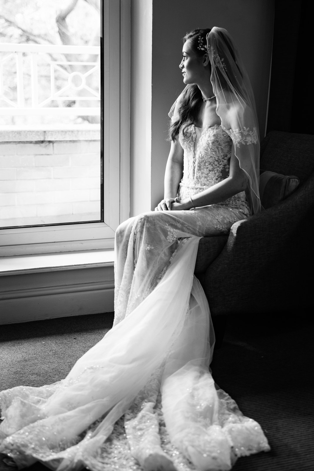 Black and white portrait of the bride seated by the window, train spilling out