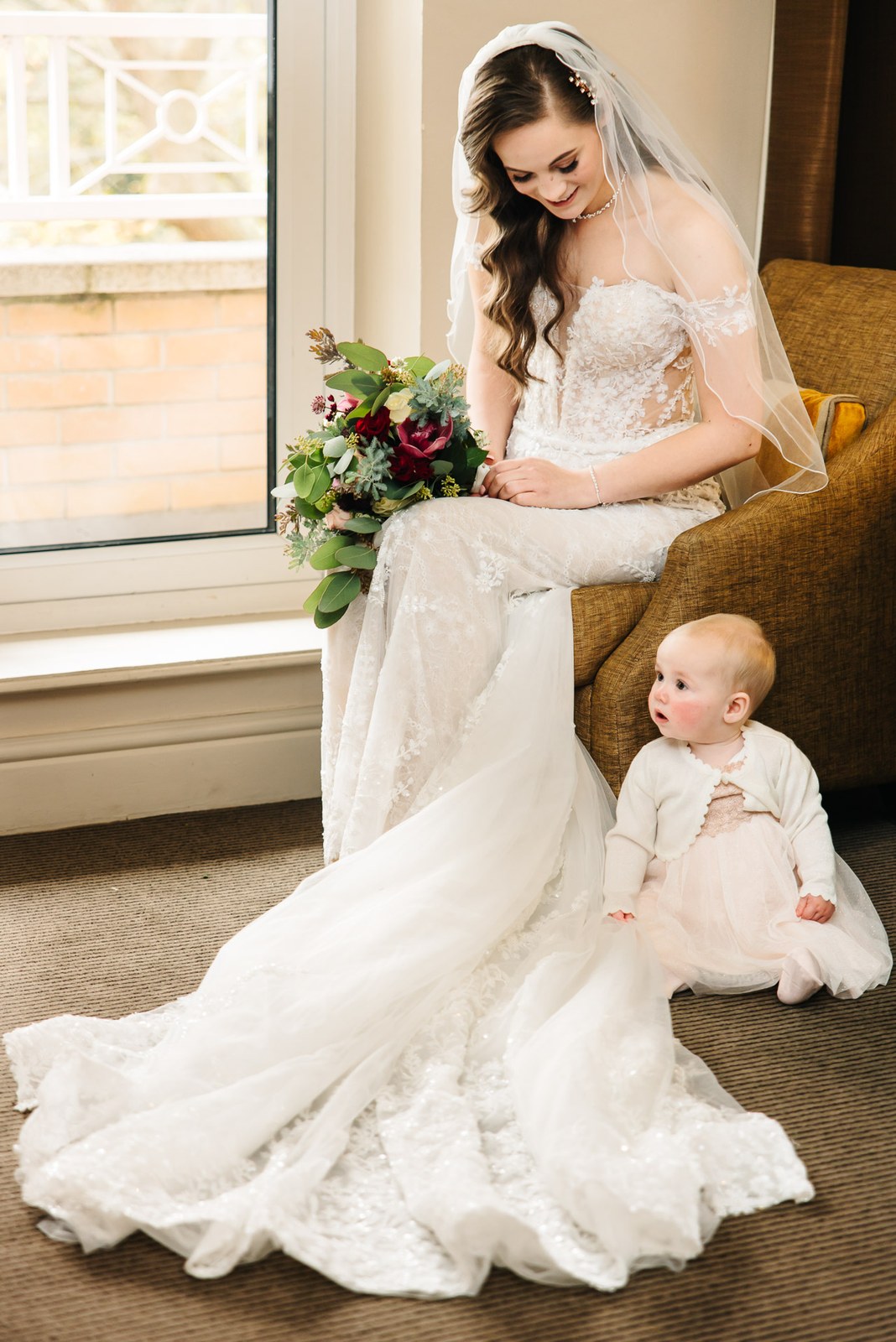 Bride seated with her bouquet beside a small child in white