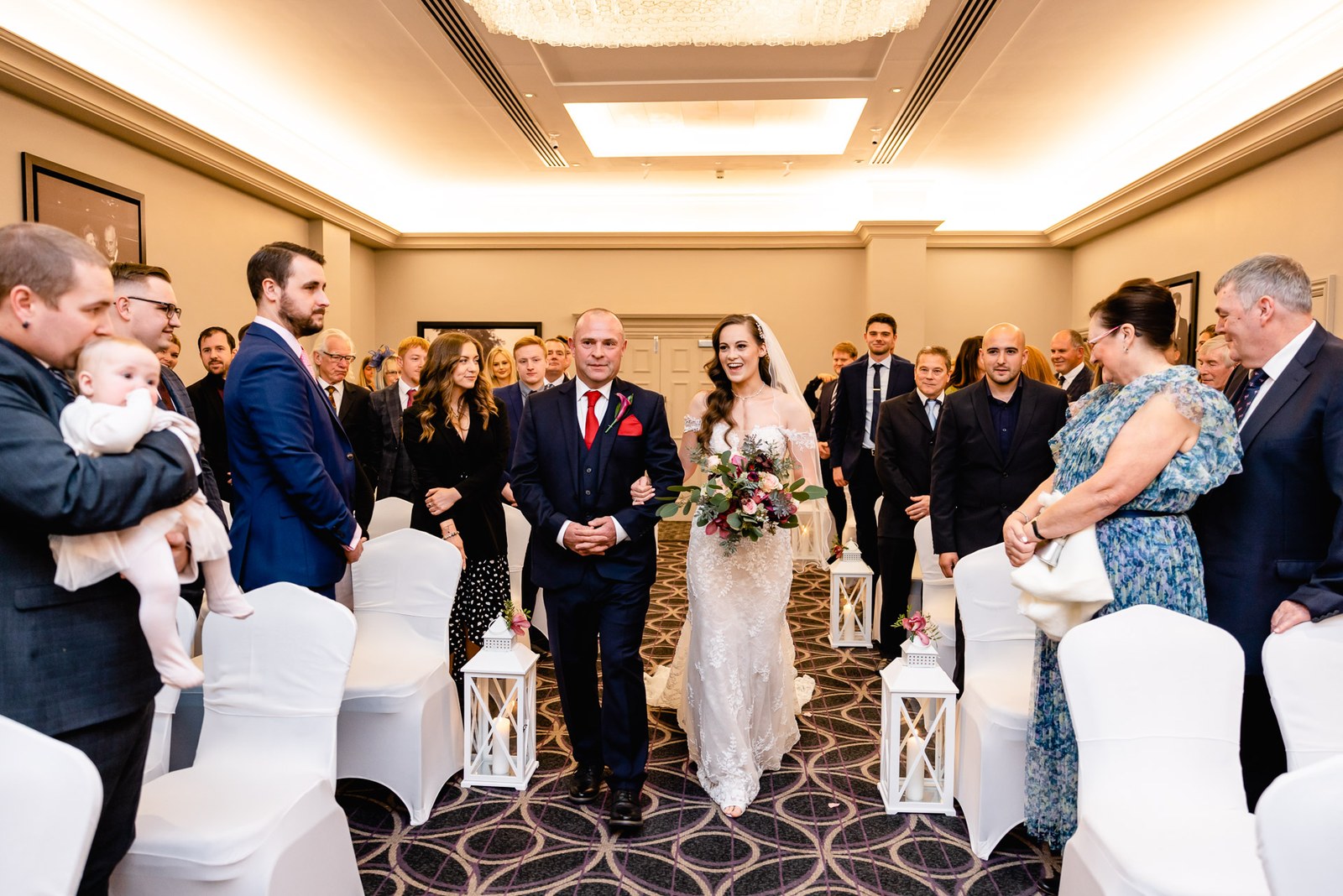 Bride on her father's arm walks the aisle as standing guests turn to watch
