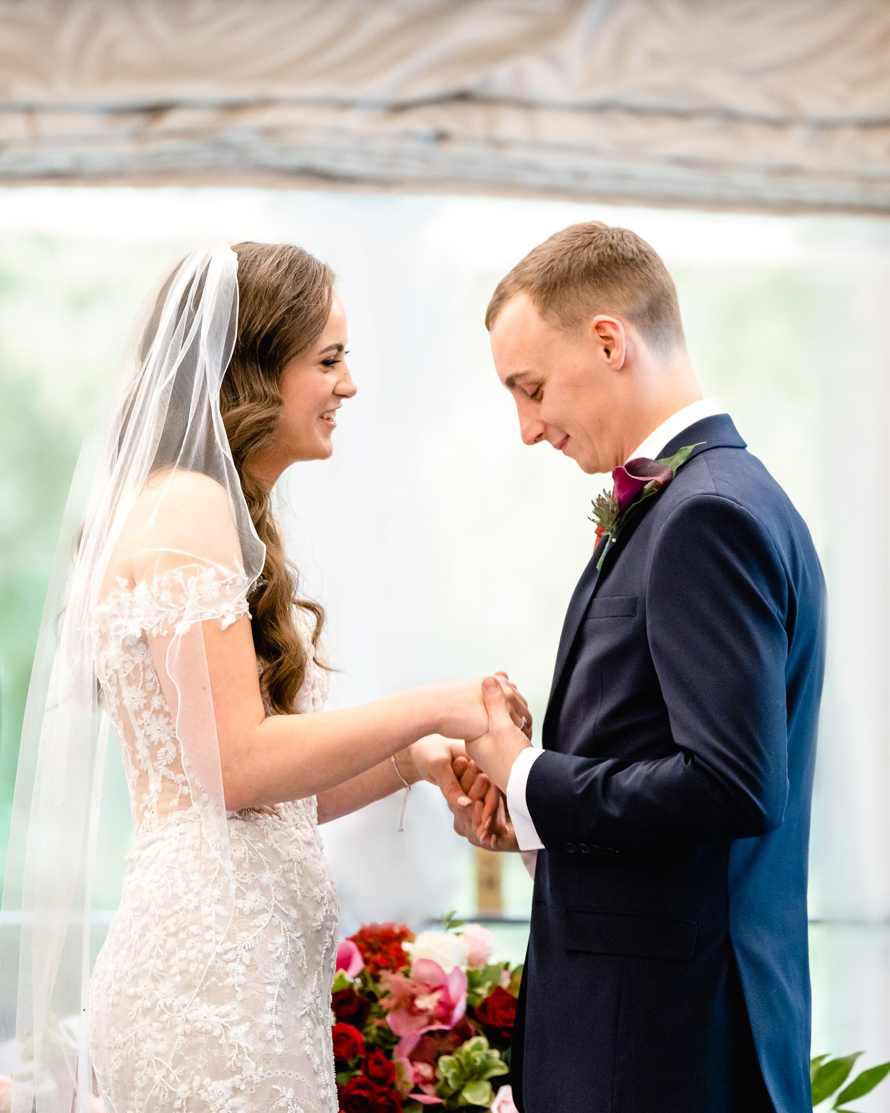 Bride and groom clasp hands, her veil framing them during the ceremony