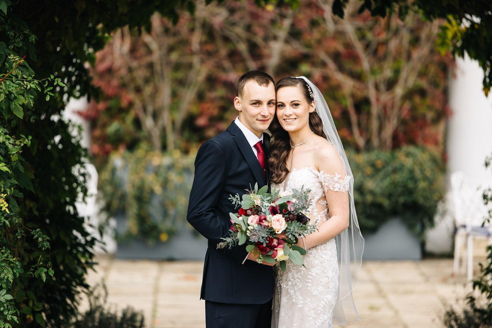 The couple embrace beneath an archway of autumn foliage in the Sopwell House grounds