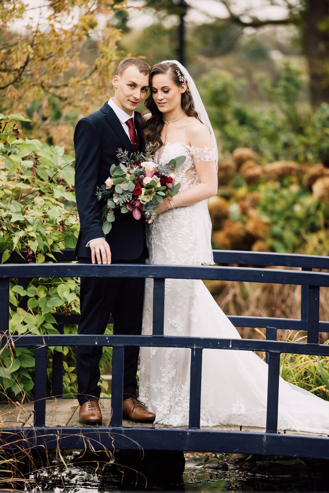 Bride and groom pause on a blue footbridge over water in the Sopwell House gardens