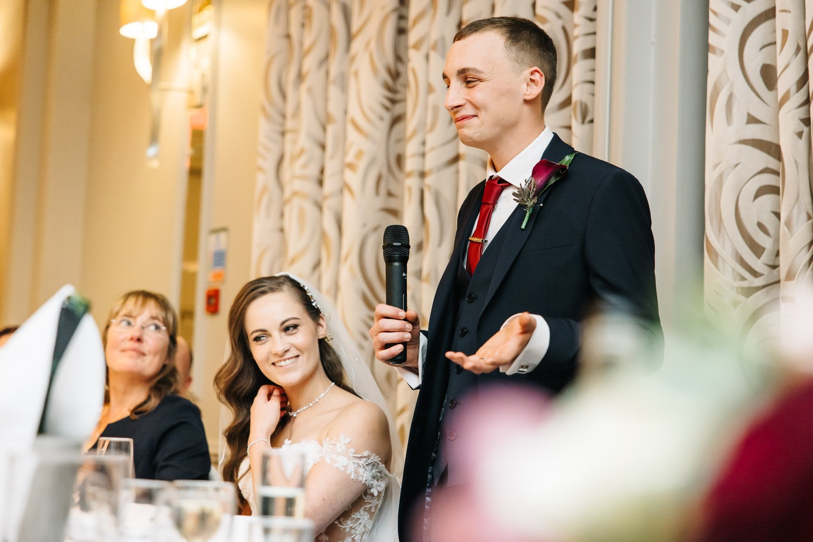 Groom speaks into a microphone as the bride smiles up at him