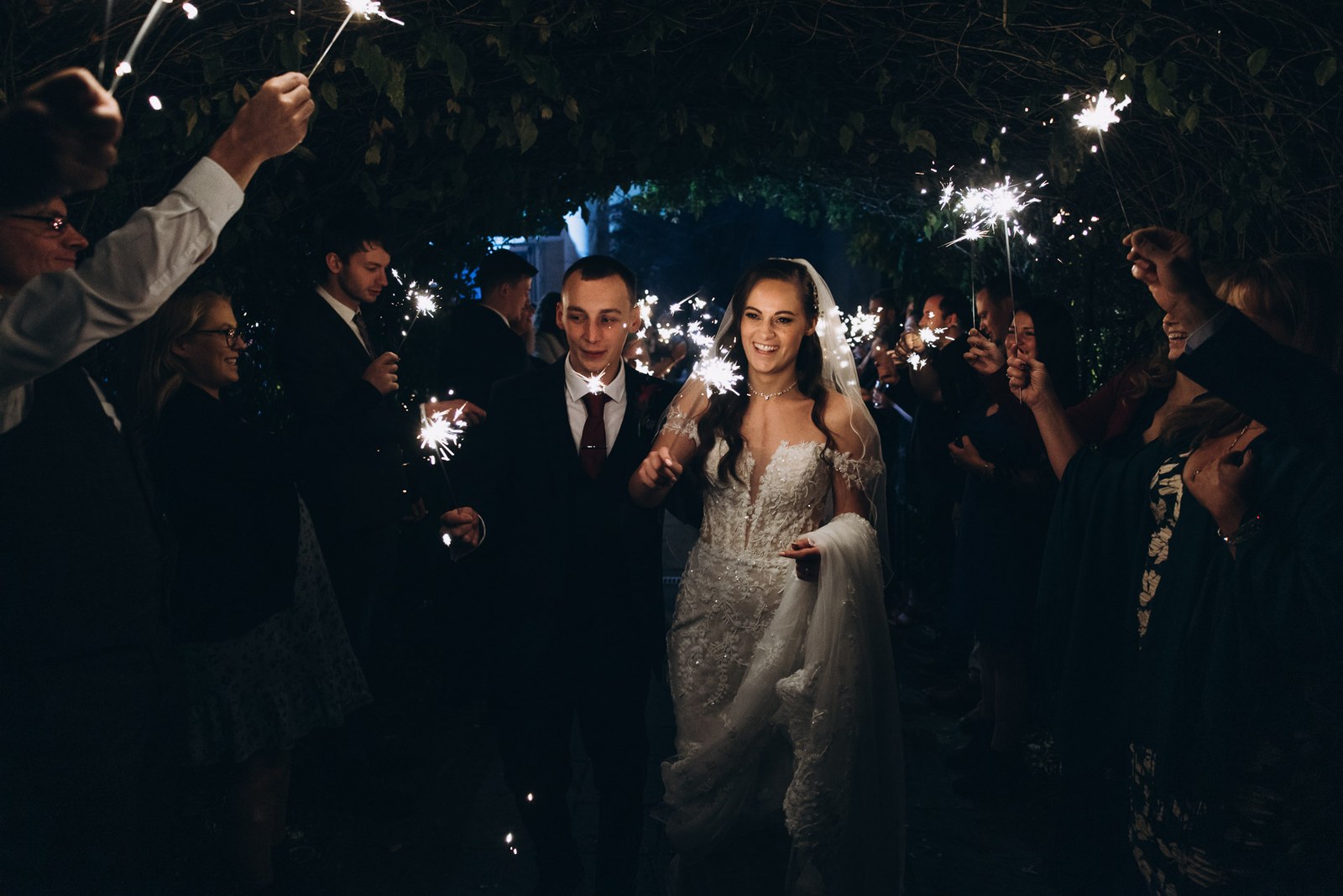 Bride and groom walk a tunnel of sparklers held by cheering guests