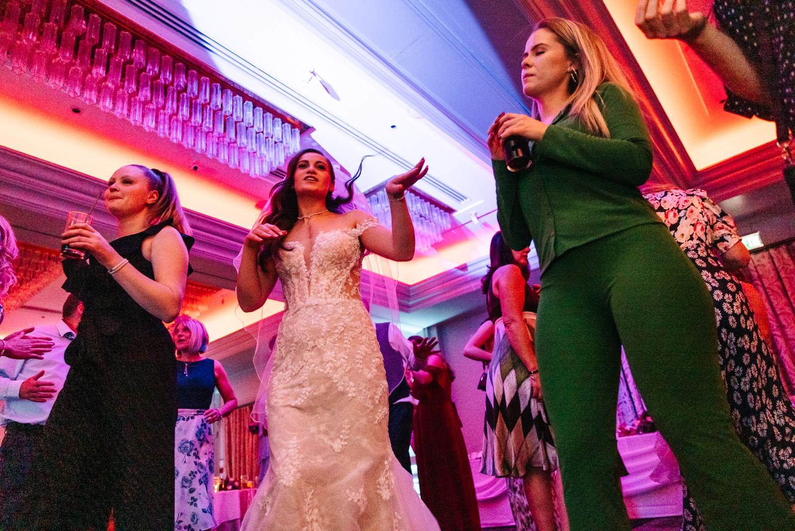 Bride dances beneath pink and purple lighting with guests around her