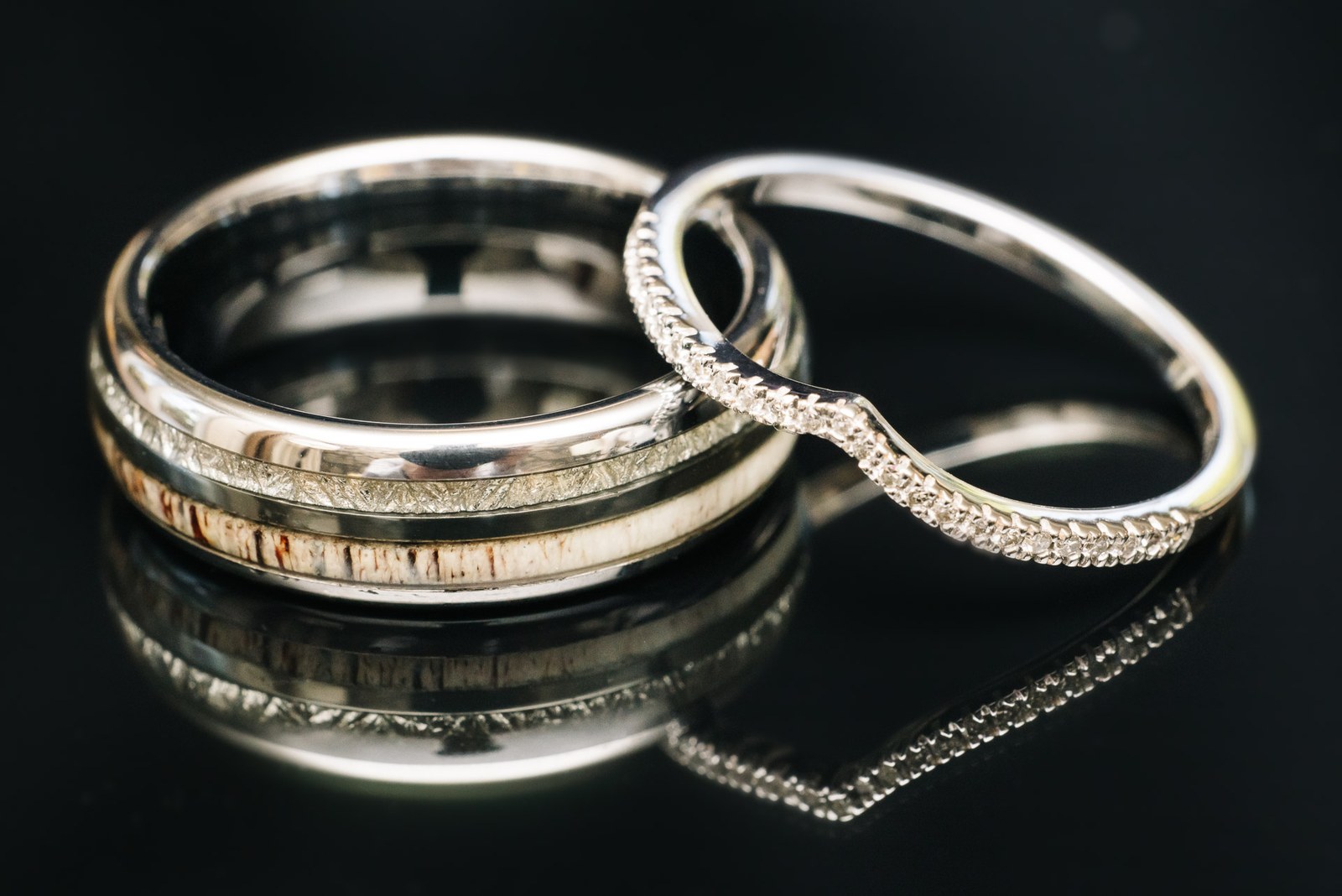 A diamond band nested against a patterned wedding ring on dark glass