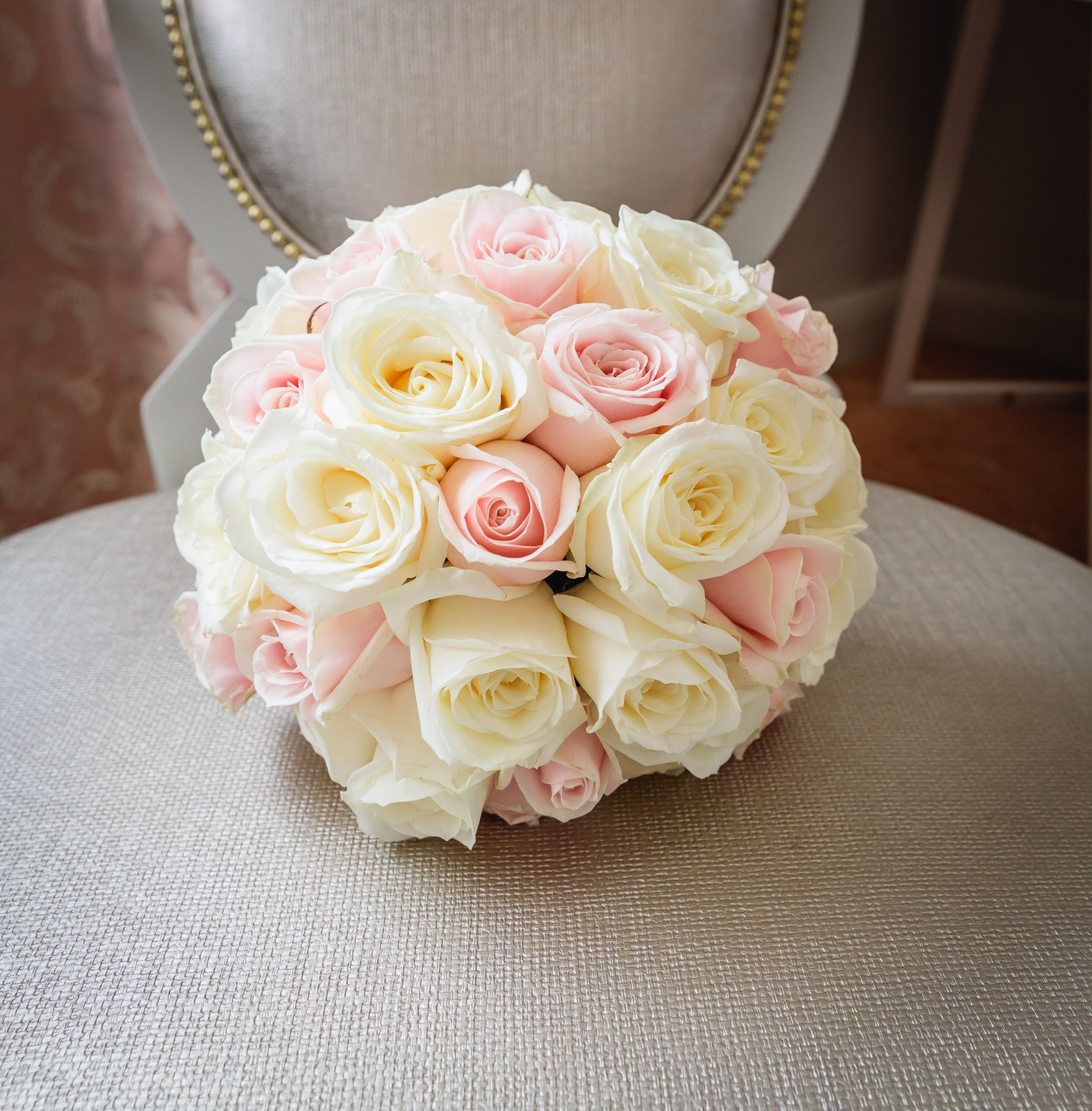 A neat posy of cream and blush roses resting on an upholstered chair