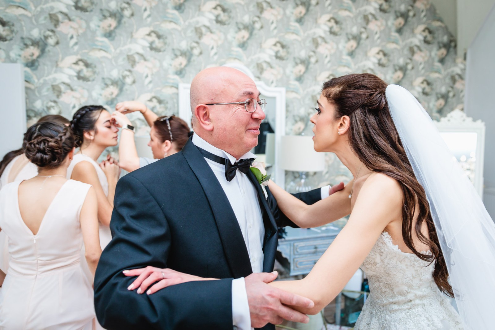 The bride straightens her father's buttonhole as the bridesmaids get ready behind