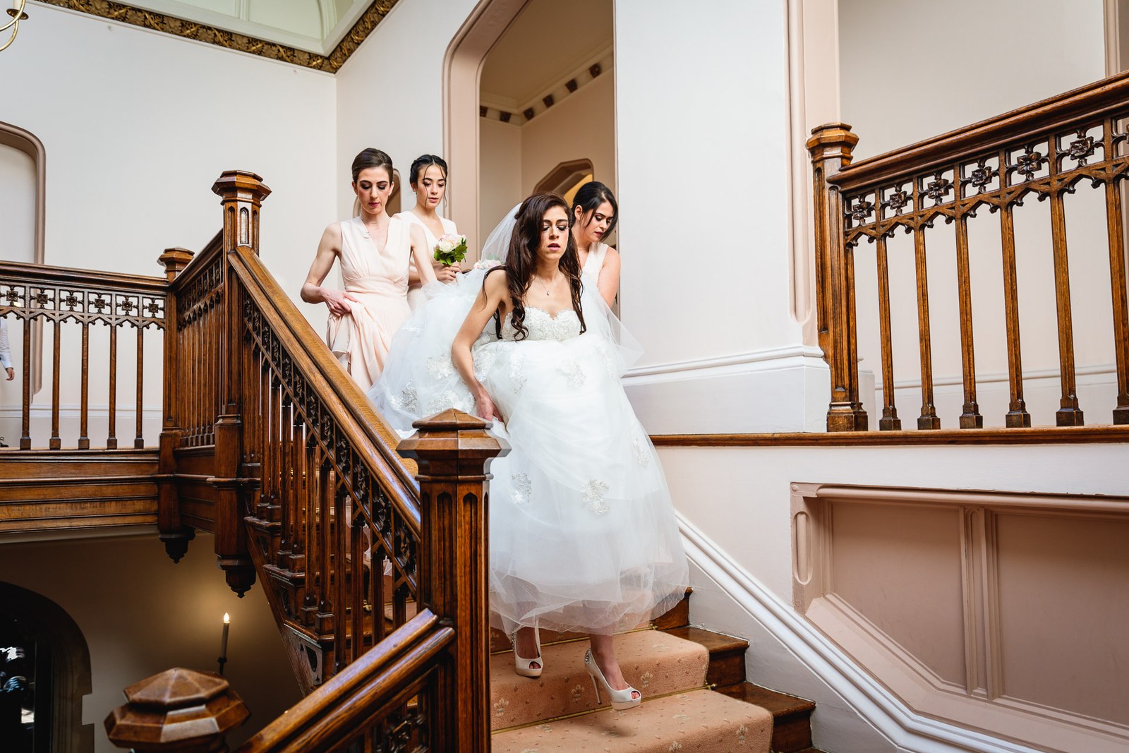 Bride descends the grand wooden staircase at St Audries Park with her bridesmaids