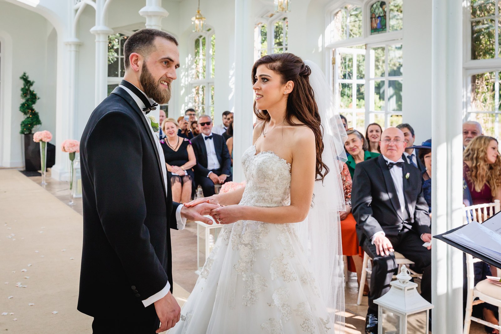 Bride and groom clasp hands as seated guests watch the ceremony